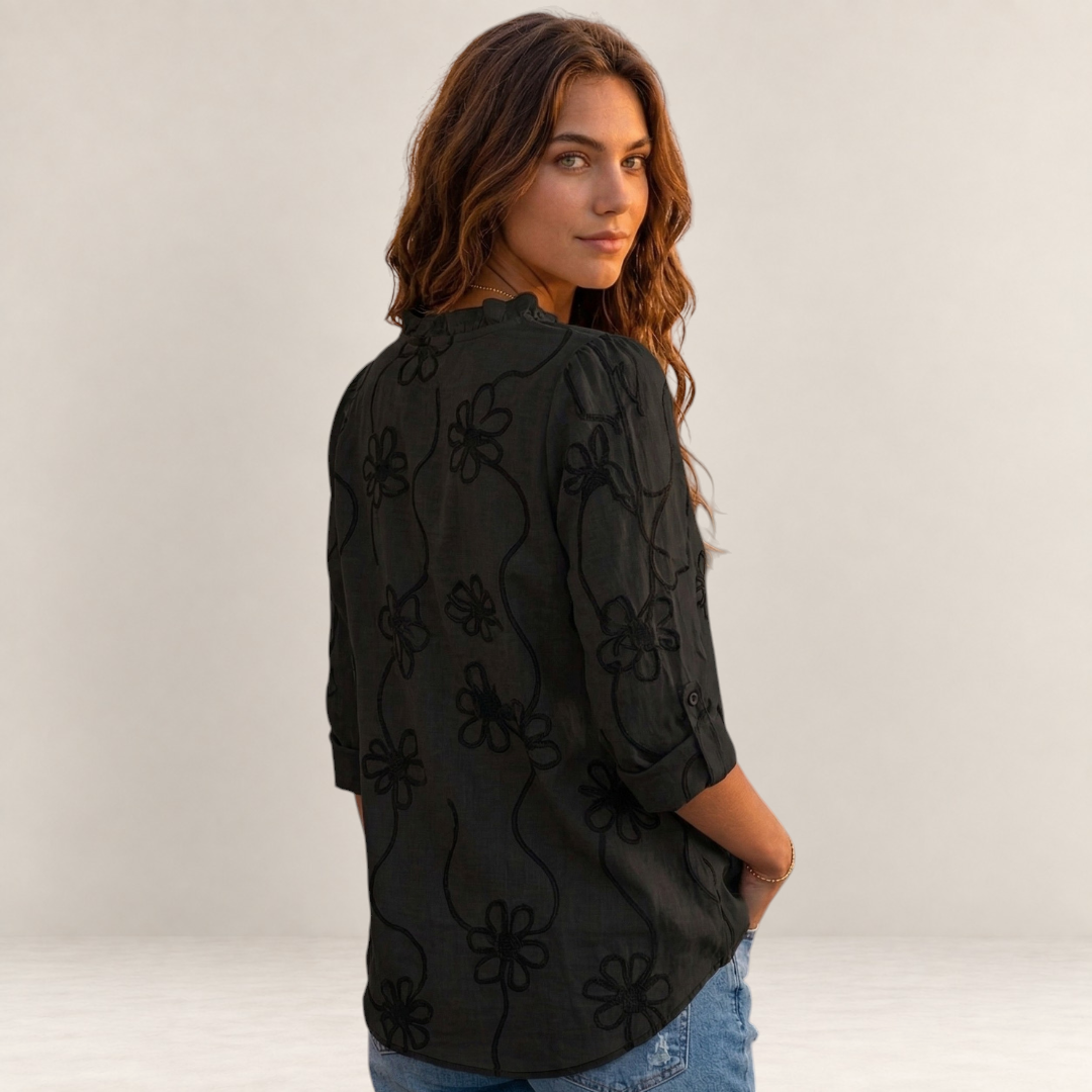 Valvet Oak House Larissa black blouse with floral embroidery worn by a woman on a sunny Mediterranean street