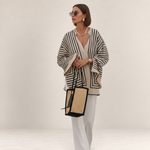 Valvet Oak House Thetis striped blouse with a relaxed flowing fit, worn with white trousers and a straw tote bag.