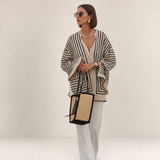 Valvet Oak House Thetis striped blouse with a relaxed flowing fit, worn with white trousers and a straw tote bag.
