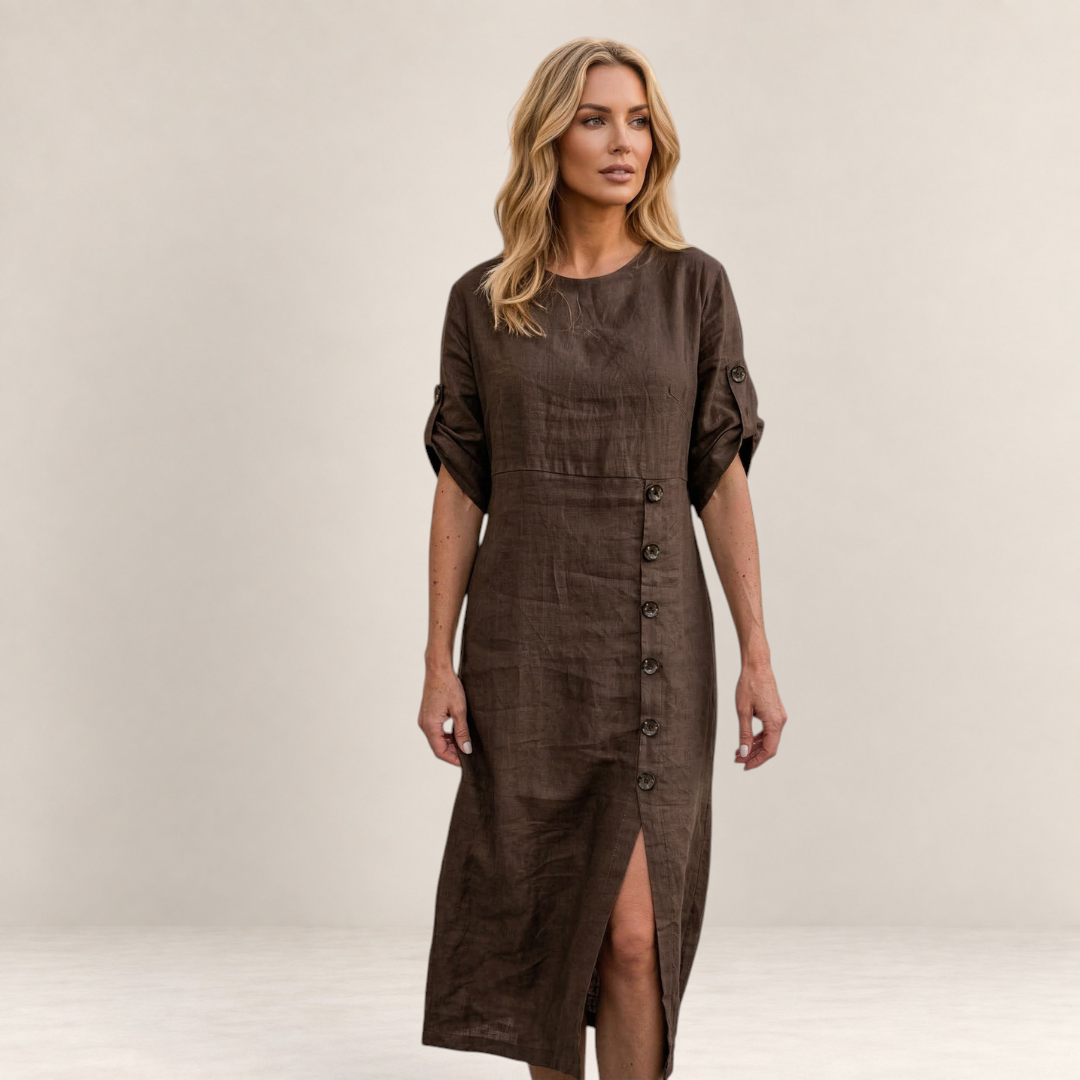 Valvet Oak House Helena brown linen midi dress with button detail and side slit worn by a blonde woman in a village