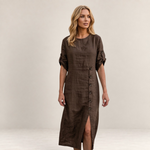 Valvet Oak House Helena brown linen midi dress with button detail and side slit worn by a blonde woman in a village