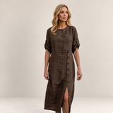 Valvet Oak House Helena brown linen midi dress with button detail and side slit worn by a blonde woman in a village