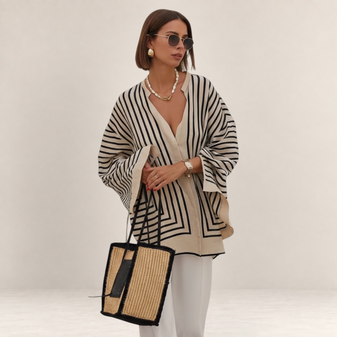 Valvet Oak House Thetis striped blouse with a flowing fit, V-neck, and wide sleeves worn by a woman with a straw bag.