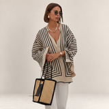 Valvet Oak House Thetis striped blouse with a flowing fit, V-neck, and wide sleeves worn by a woman with a straw bag.
