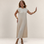 Valvet Oak House Chrysanthe cream pleated midi dress worn by a woman in a scenic Mediterranean street at sunset
