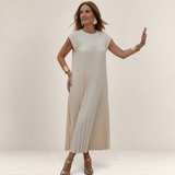 Valvet Oak House Chrysanthe cream pleated midi dress worn by a woman in a scenic Mediterranean street at sunset