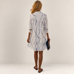 Back view of a woman wearing a Valvet Oak House white shirt dress with a blue wavy line pattern and A-line cut.