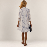 Back view of a woman wearing a Valvet Oak House white shirt dress with a blue wavy line pattern and A-line cut.
