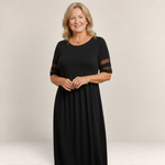 Valvet Oak House Penelope black maxi dress with sheer sleeve details worn by a smiling woman in a Mediterranean street