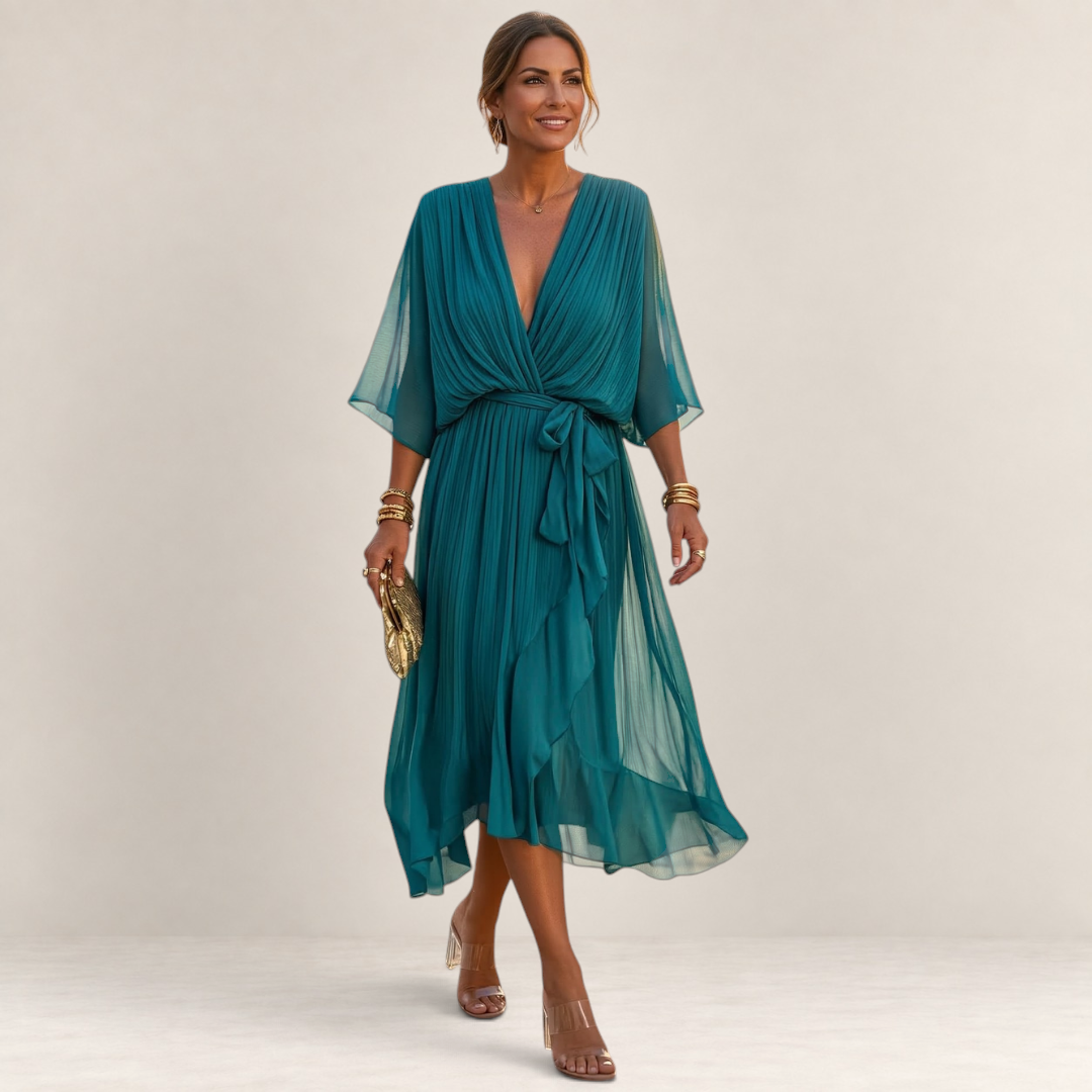 Valvet Oak House Helena teal pleated midi dress with V-neck and waist tie worn by a woman on a cobblestone street