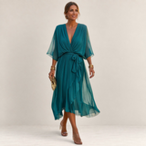 Valvet Oak House Helena teal pleated midi dress with V-neck and waist tie worn by a woman on a cobblestone street