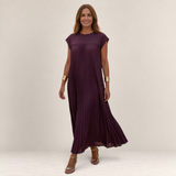 Valvet Oak House Chrysanthe elegant dark purple pleated midi dress worn by a woman on a cobblestone street at sunset