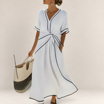 Valvet Oak House Mila white midi dress with V-neck, black contrast trim, and waist detail, worn by a woman by the sea.