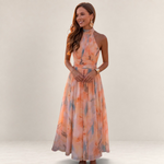 Valvet Oak House silk maxi dress with halter neckline in a peach floral print, worn by a woman at sunset in Greece.