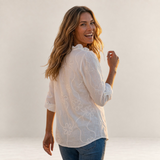 Valvet Oak House Larissa white floral embroidered blouse worn by a smiling woman in a scenic Mediterranean village