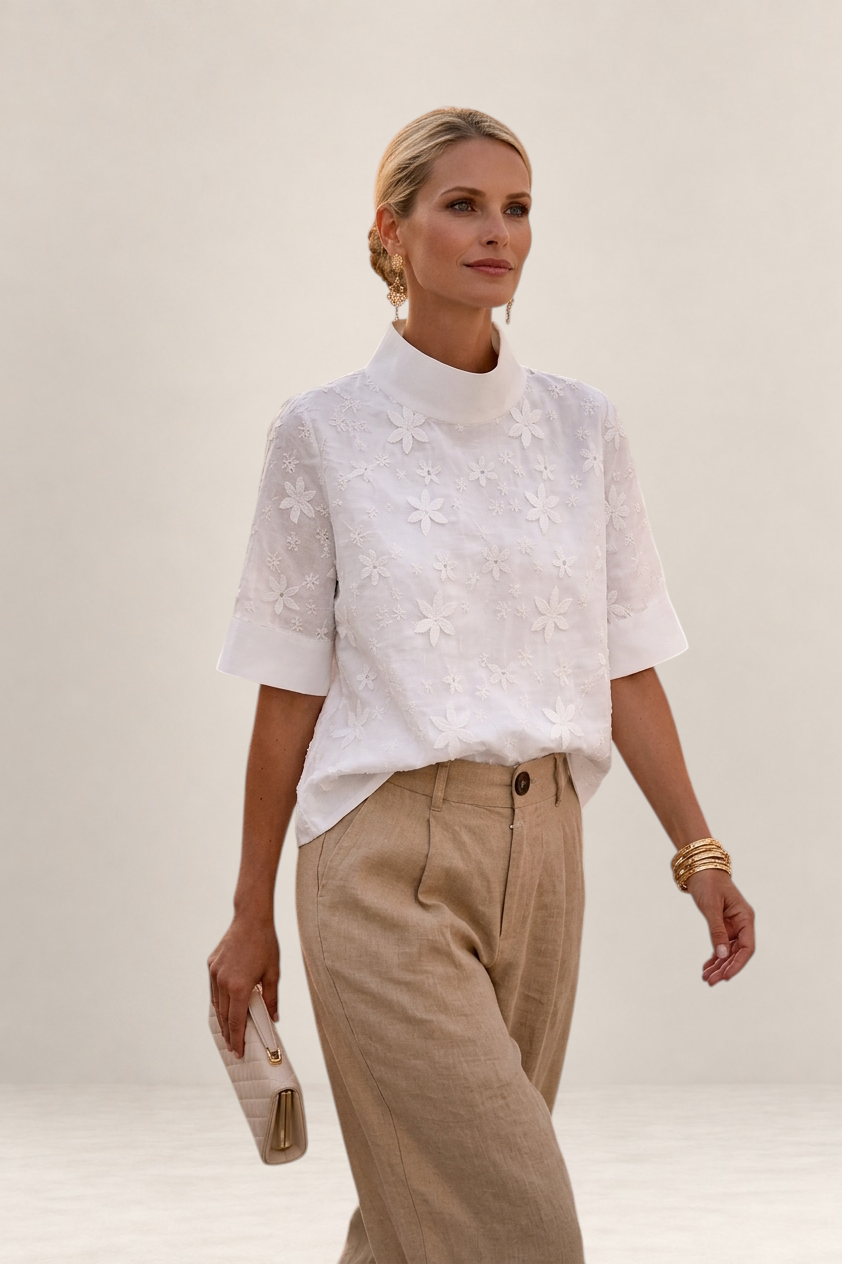 Valvet Oak House white floral embroidered blouse with high neck and short sleeves worn by a woman with beige trousers.