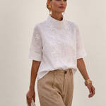 Valvet Oak House white floral embroidered blouse with high neck and short sleeves worn by a woman with beige trousers.