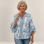 Valvet Oak House Agapi blouse with blue and white leaf print, V-neck, and ruffled sleeves worn by a smiling woman.