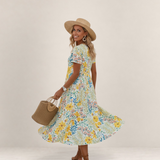 Valvet Oak House Margaret floral midi dress with short sleeves, worn by a smiling woman in a straw hat and bag