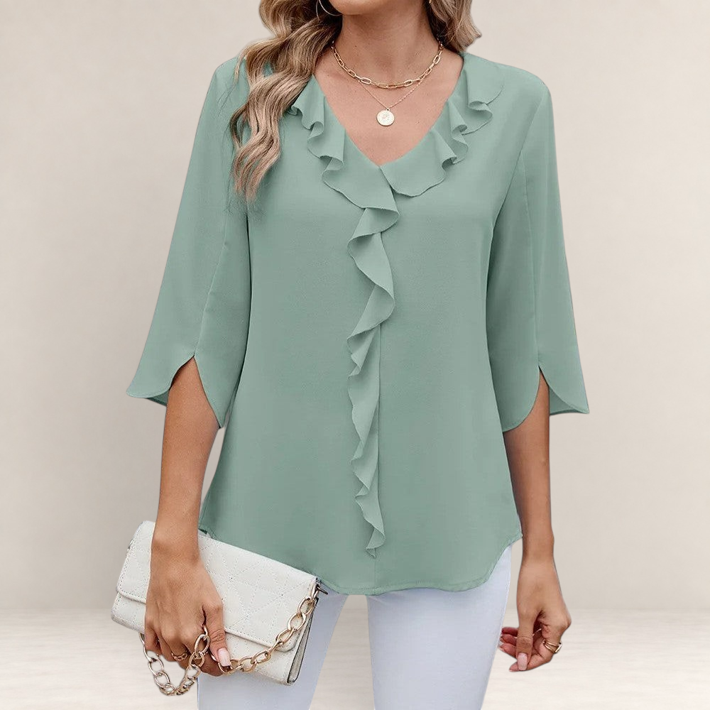 Valvet Oak House blue blouse with ruffled neckline and 3/4 sleeves, styled with white trousers and a clutch bag.