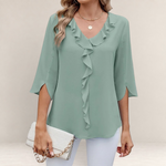 Valvet Oak House blue blouse with ruffled neckline and 3/4 sleeves, styled with white trousers and a clutch bag.