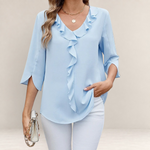 Valvet Oak House light blue blouse with ruffled neckline and 3/4 sleeves worn with white trousers