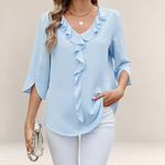 Valvet Oak House light blue blouse with V-neck, front ruffles, and 3/4 split sleeves worn with white trousers