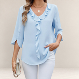 Valvet Oak House light blue blouse with V-neck, front ruffles, and 3/4 split sleeves worn with white trousers