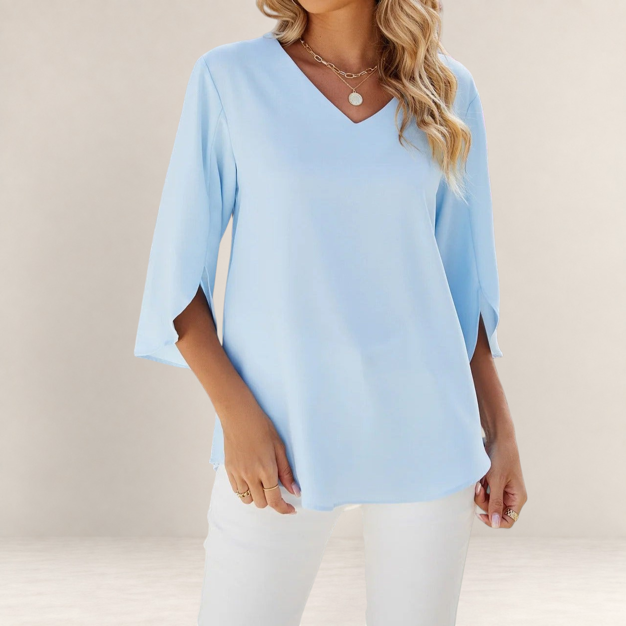 Valvet Oak House light blue blouse with V-neck, 3/4 sleeves, and elegant ruffle details worn with white trousers.