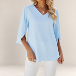 Valvet Oak House light blue blouse with V-neck, 3/4 sleeves, and elegant ruffle details worn with white trousers.